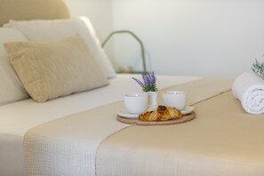 Un letto rifatto con un cuscino, un vassoio con un croissant e due tazze, e un asciugamano arrotolato.