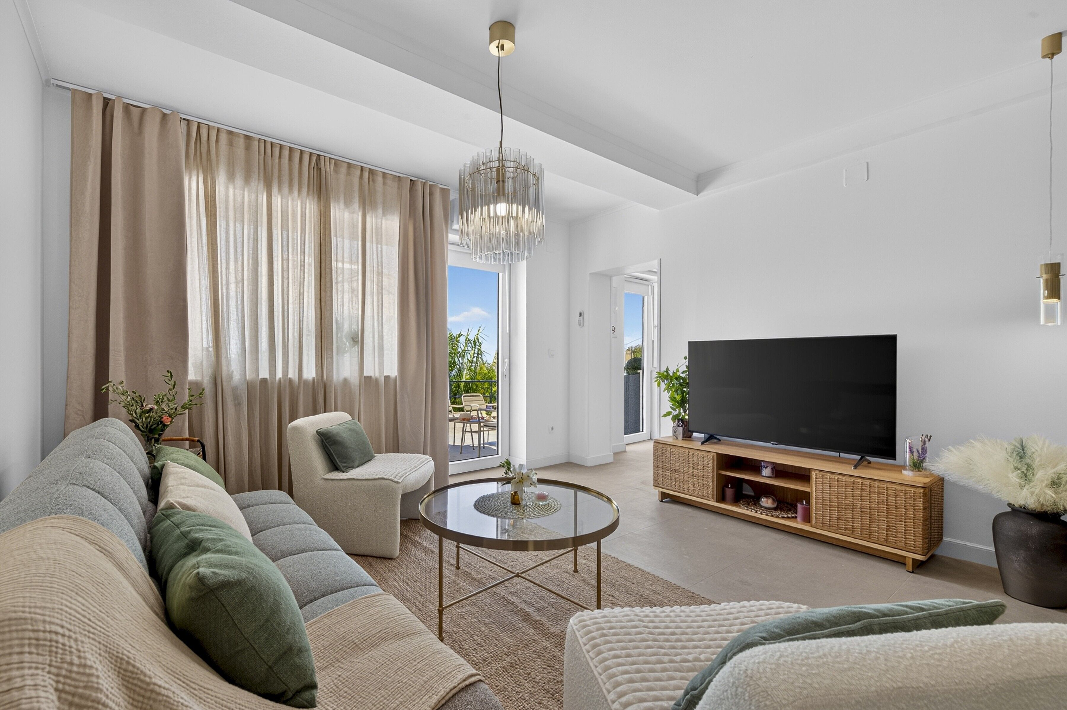 A modern living room with a sofa set, a television, and a dining area visible through a glass door.