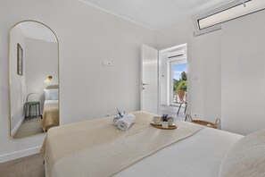 A hotel room with a bed, a mirror, a bedside table with a lamp, a window, and an open door leading to a balcony. - Two Bedroom Apartment with Terrace (Mlini)