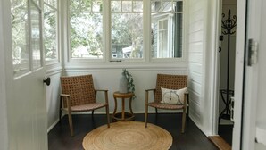 A room with two wicker chairs, a small round table, and a woven rug. - The Foxman Cottage (Broke)