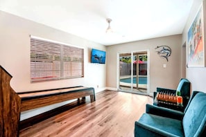 Ein Zimmer mit Holzboden, einer Bank, einem Sofa, einem Fernseher und einer Glastür, die zu einem Außenbereich führt.