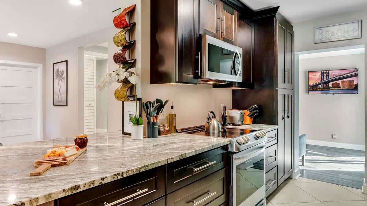 A modern kitchen with dark cabinetry, stainless steel appliances, and a marble countertop.