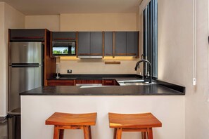 Eine moderne Küche mit einem Edelstahl-Kühlschrank, Holzschränken, einer schwarzen Arbeitsplatte und zwei Holzbarhocker.