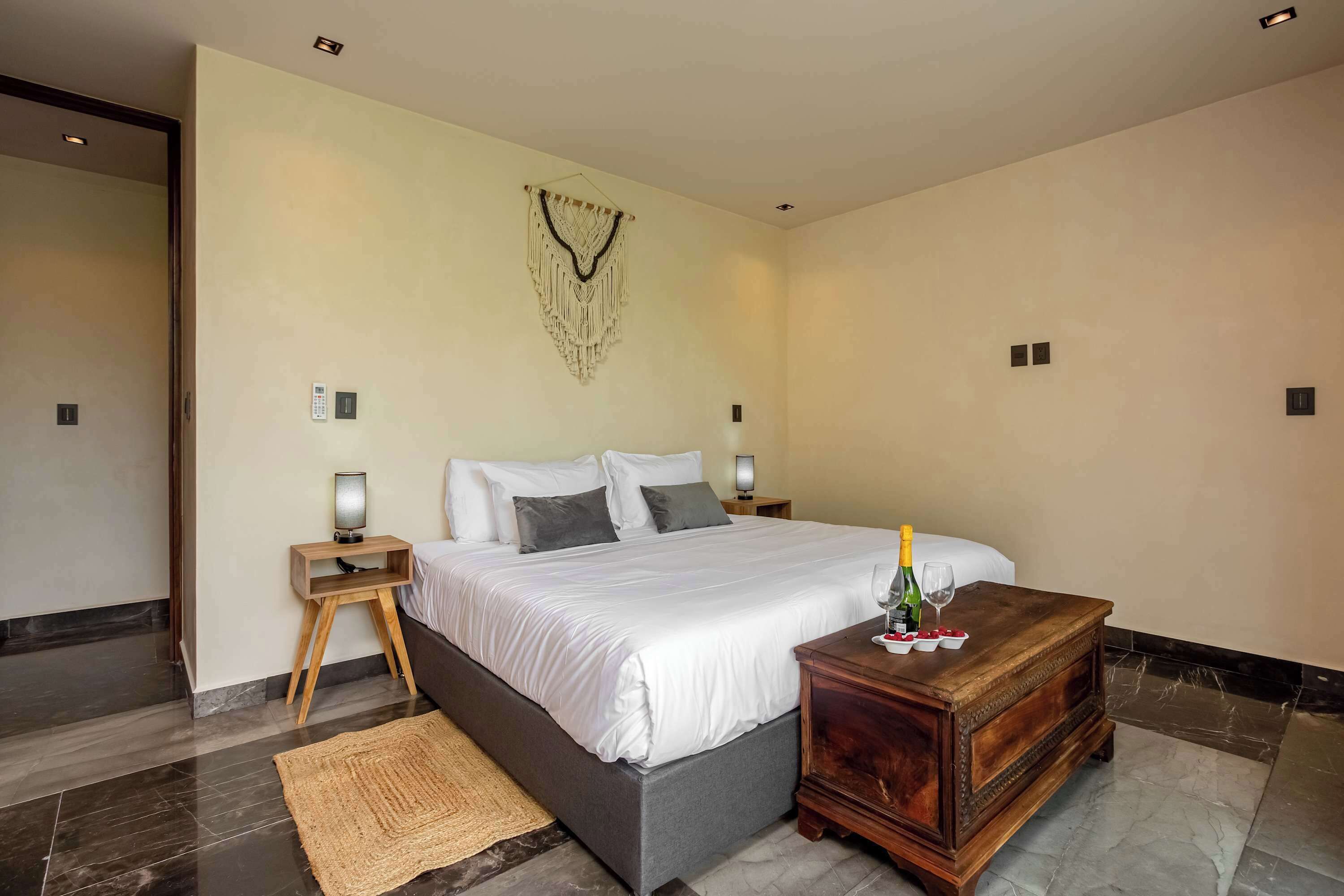 A modern bedroom with a large bed, bedside lamps, a wooden nightstand, a woven rug, and a wooden dresser.