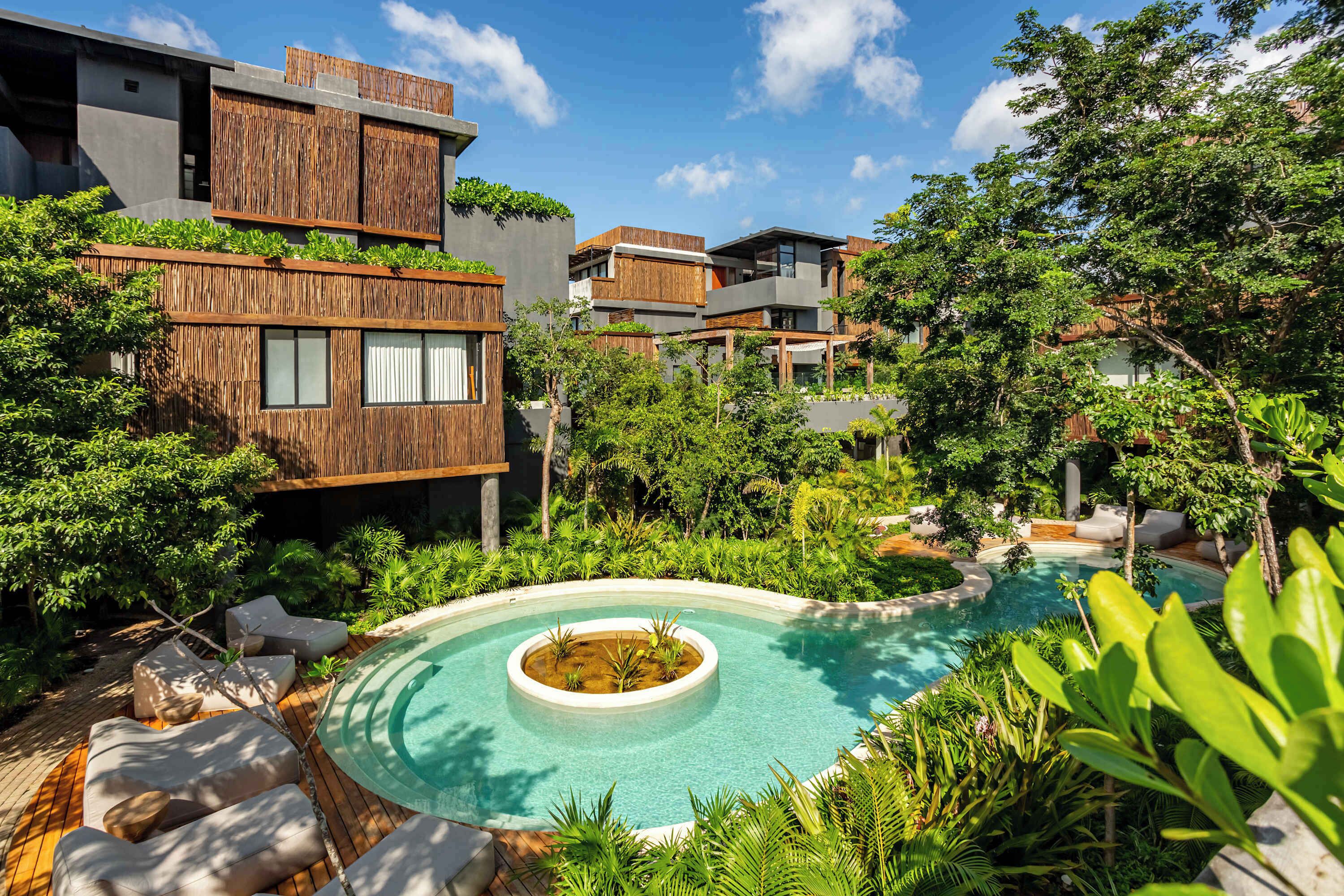 A modern residential complex with a central swimming pool, surrounded by lush greenery and contemporary architecture.