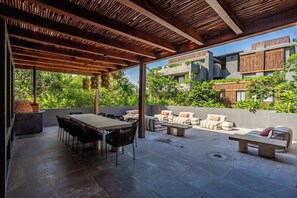 Eine Terrasse im Freien mit einer Holzhütte, einem Esstisch mit Stühlen und einer Sitzecke mit Sofas und Kissen.