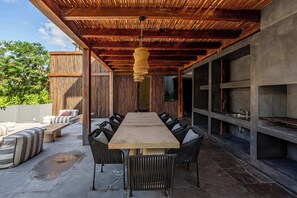 An outdoor patio with a long wooden table and chairs, a hanging light fixture, and a view of greenery. - Modern 1BR Jungle View Retreat in Humana | Rooftop (Tulum)