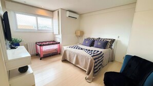 Une chambre à coucher de taille réduite, comprenant un lit, une table de chevet, une chaise, un radiateur, une fenêtre et un appareil de climatisation.