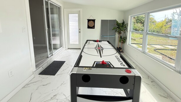 Ein Zimmer mit Fußballtisch, Schiebetür, Dartscheibe und Blick ins Freie.