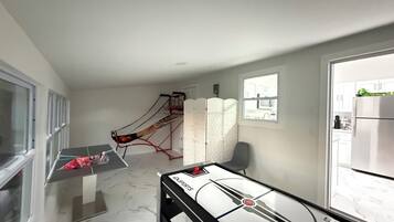 Una habitación con mesa de ping pong, una pequeña zona de estar y vista a la cocina a través de una ventana.