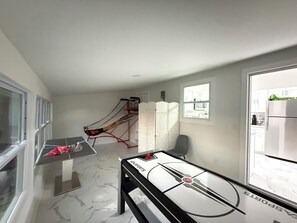 Una habitación con mesa de ping pong, una pequeña zona de estar y vista a la cocina a través de una ventana.
