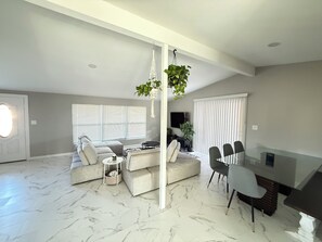 Una sala de estar moderna con un sofá seccional, una mesa de comedor con sillas y una planta colgante.