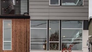 A multi-story residential building with a modern architectural design, featuring a combination of wood and metal materials, large windows, and a visible balcony on the upper floor. - Modern 3 Bedroom Townhouse w/ Private Rooftop (Seattle)