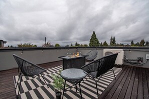Eine Dachterrasse mit Schachbrettboden, einer Feuerstelle und Gartenmöbeln.