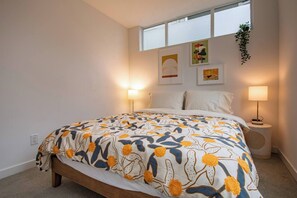 A bedroom with a bed, two bedside lamps, a window, and wall art.