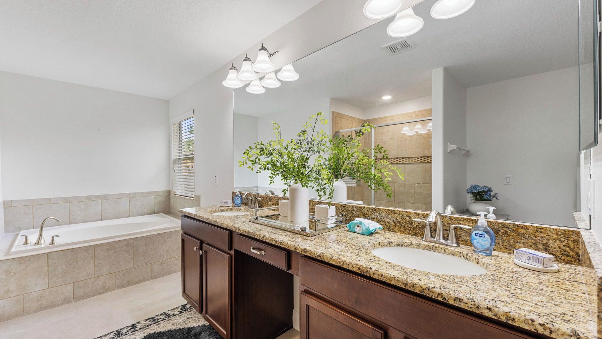 A modern bathroom with a double sink vanity, a large mirror, and a shower area.
