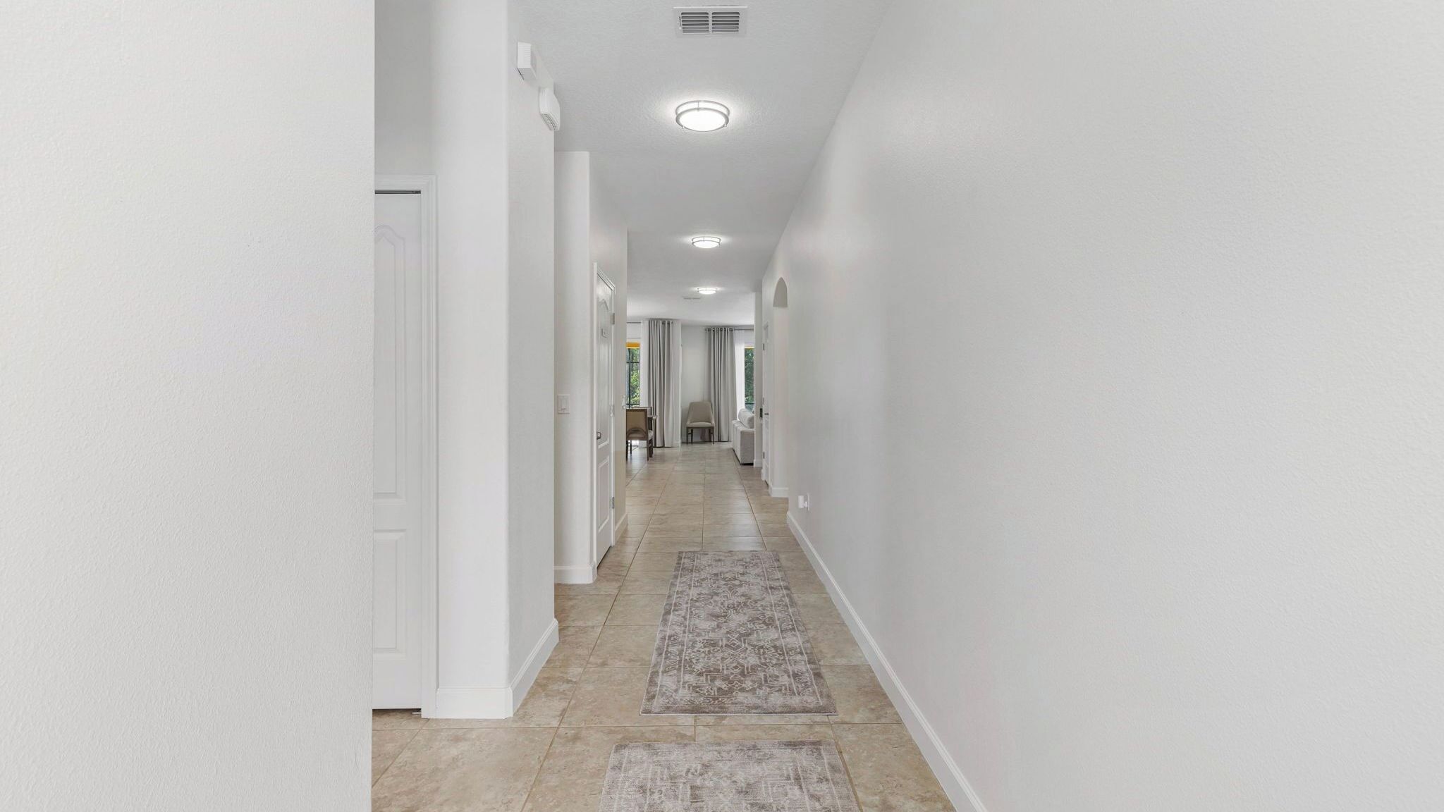 Un pasillo con paredes blancas, piso de baldosas y un tapete que lleva a una habitación con puerta.