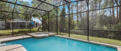 A swimming pool with a glass enclosure, surrounded by a forested area.
