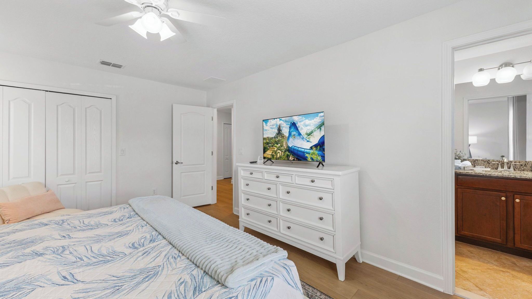 Un dormitorio con cama, cómoda, televisor y baño con espejo y lavabo.