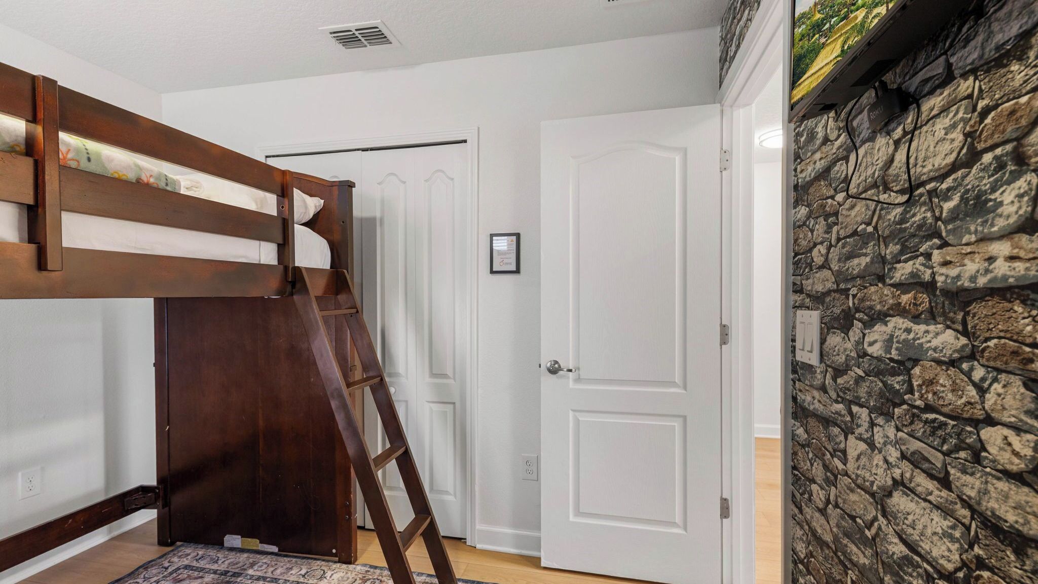 A room with a bunk bed, a white door, and a stone wall.