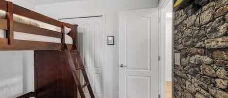 A room with a bunk bed, a white door, and a stone wall.