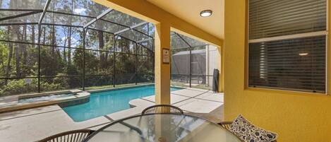 A glass-enclosed outdoor pool area with a hot tub, surrounded by a yellow wall and a view of a forest.