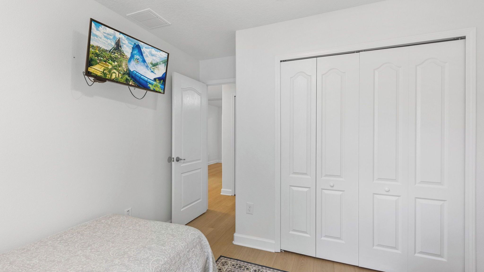 Une chambre à coucher avec un lit, un téléviseur fixé au mur et une armoire blanche.