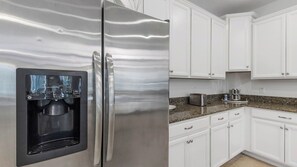 Ein Kühlschrank aus Edelstahl mit Wasserspender, weiße Schränke, eine Arbeitsplatte aus Granit und ein Toaster.