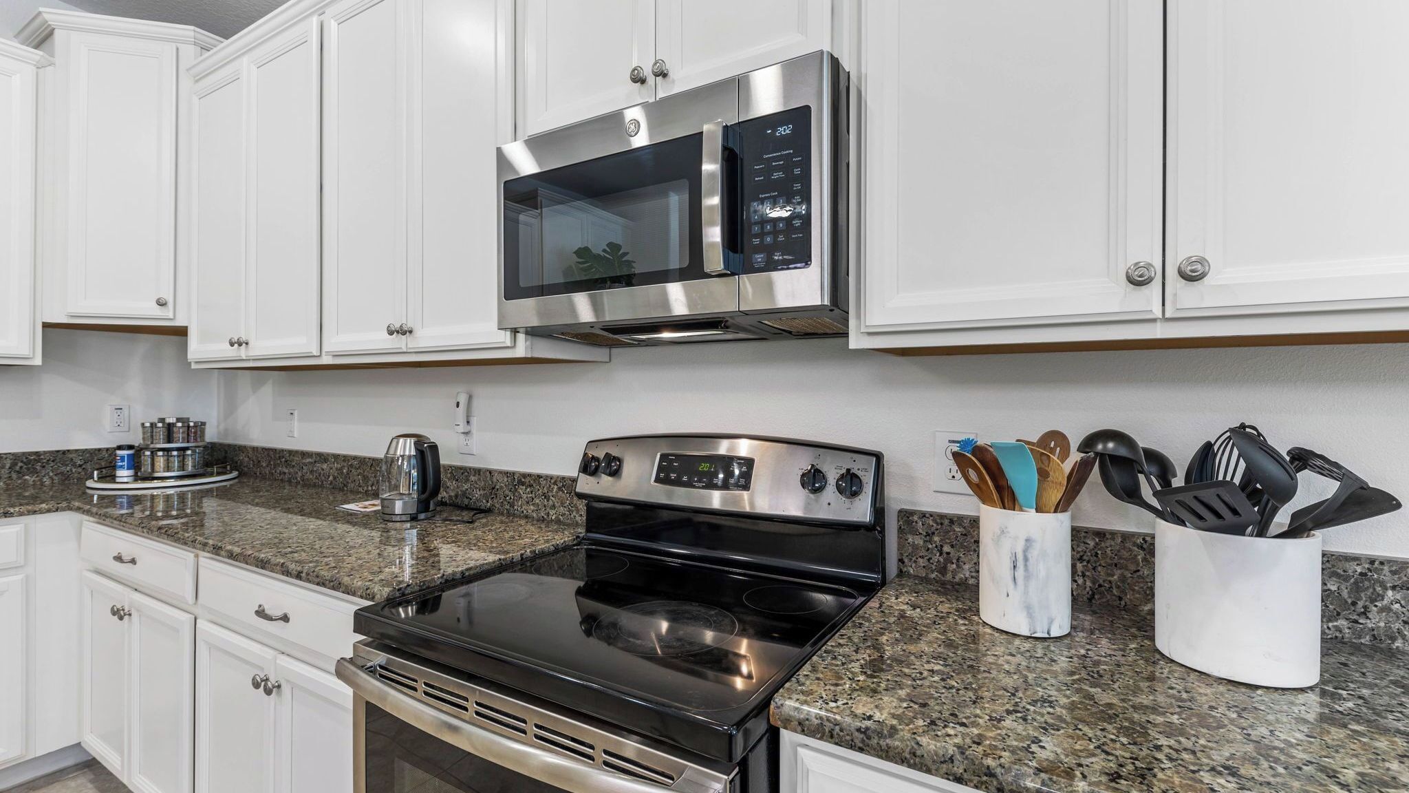A kitchen with white cabinets, a stainless steel microwave, a stove, and a coffee maker.