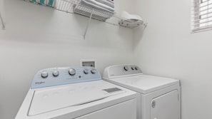 Ein Waschbereich mit einer Whirlpool Waschmaschine und einem Trockner, einer weißen Wand und einem Regal mit Handtüchern.