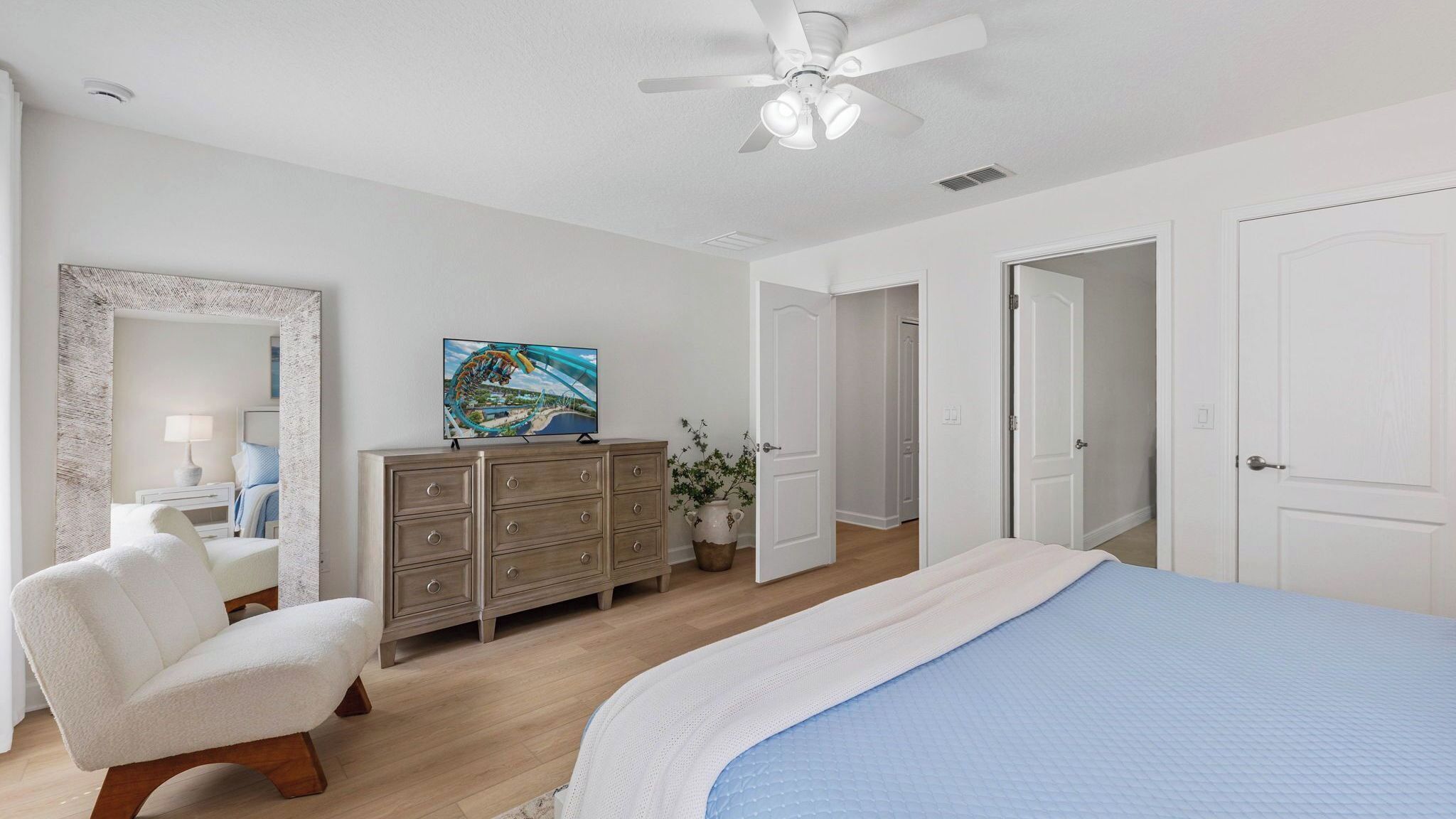 A bedroom with a bed, a dresser, a chair, a ceiling fan, and a painting on the wall.