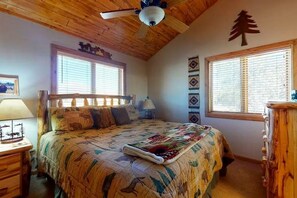 A bedroom with a wooden ceiling, a bed with a quilt, two bedside tables, and a window with blinds. - 4BR Riverfront | Hot Tub | Fireplace (South Fork)