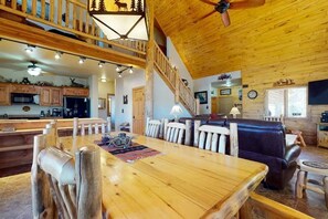 A spacious living area with a wooden dining table, a sofa, and a staircase leading to an upper level. - 4BR Riverfront | Hot Tub | Fireplace (South Fork)