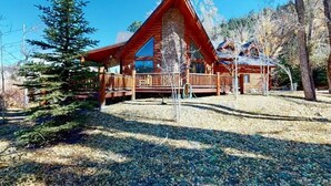 A log cabin with a stone foundation, wooden deck, and a large window. - 4BR Riverfront | Hot Tub | Fireplace (South Fork)
