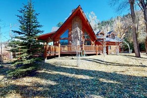 A log cabin with a stone foundation, wooden deck, and a large window. - 4BR Riverfront | Hot Tub | Fireplace (South Fork)