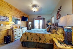 Ein Schlafzimmer mit Holzwand, einem Bett mit gemustertem Überwurf, einem Schminktisch, einem Fernseher und einem Deckenventilator.