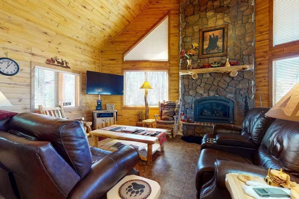 A cozy cabin interior with a stone fireplace, leather sofas, a television, and a clock on the wall.