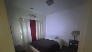 A bedroom with a bed, a nightstand, a lamp, and a red curtain.