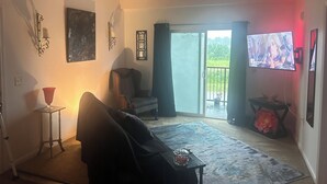 A living room with a sofa, a coffee table, a television, and a sliding glass door leading to a balcony.