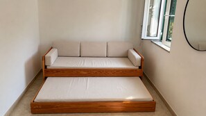 Un sofá cama convertible con estructura de madera y cojines beige en una habitación con ventana.