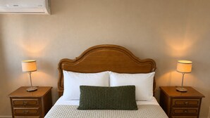 Une chambre d’hôtel avec une tête de lit en bois, deux tables de chevet avec des lampes, un lit avec une literie blanche et un coussin décoratif vert.