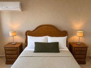 Habitación de hotel con cabecera de madera, dos mesitas de noche con lámparas, cama con ropa blanca y un cojín verde.