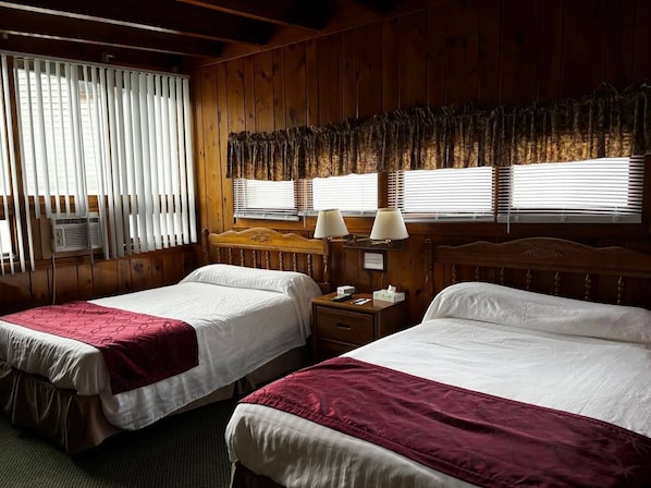 A hotel room with two beds, wooden paneling, a window with blinds, and a nightstand with a lamp. - Cozy 1-bedroom hotel room, Hamilton - #351 Oneida (Hamilton)