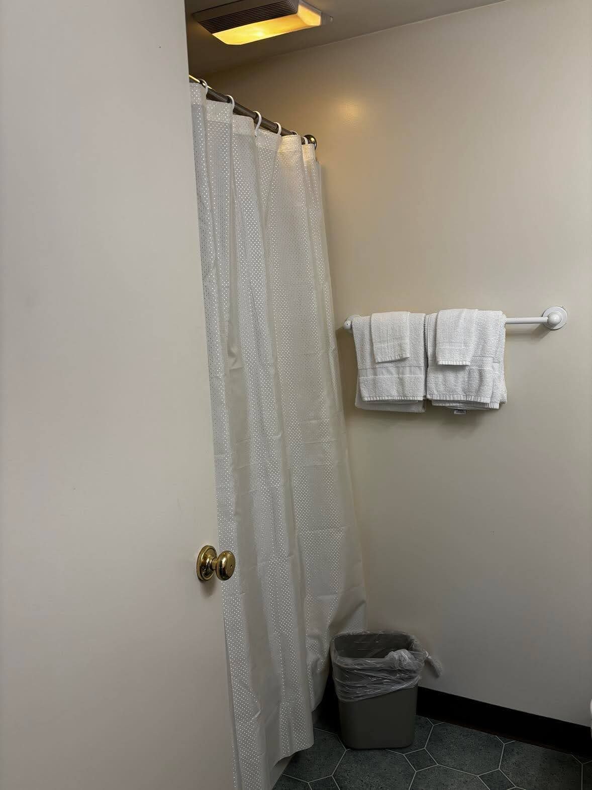 Uma casa de banho com cortina de chuveiro, porta-toalhas com toalhas e um cestinho de lixo.