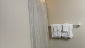 Uma casa de banho com cortina de chuveiro, porta-toalhas com toalhas e um cestinho de lixo.