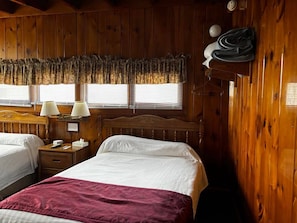 A wooden cabin room with two beds, a nightstand with a lamp, and a window with blinds. - Cozy 1-bedroom hotel room, Hamilton - #351 Oneida (Hamilton)