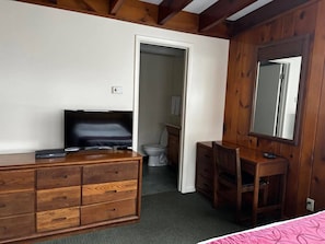 A bedroom with a wooden dresser, a television, a desk, and a mirror. There is a door leading to a bathroom. - Cozy 1-bedroom hotel room, Hamilton - #351 Oneida (Hamilton)