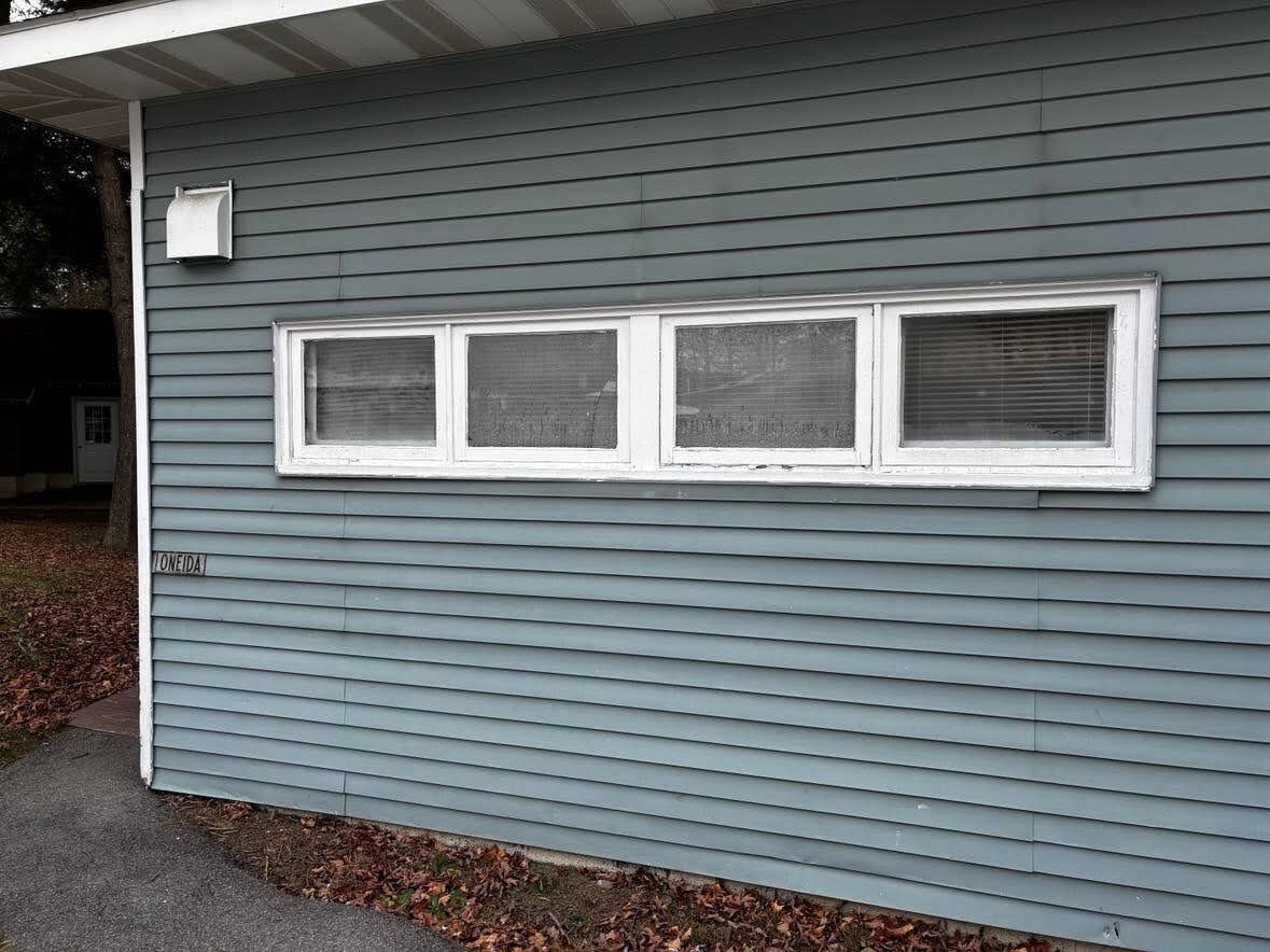Ett hus med grå ytterpanel, en inglasad veranda och ett fönster med persienner.