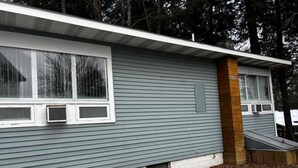 Een gelijkvloers huis met grijze gevelbekleding, een klein voortort en een zichtbaar raam.