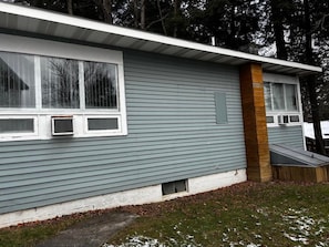 A single-story house with a grey siding exterior, a small front porch, and a visible window. - Cozy 1-bedroom hotel room, Hamilton - #351 Oneida (Hamilton)